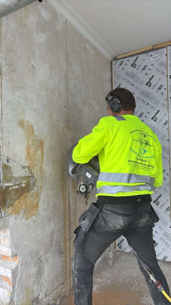 Medarbejder udfører diamantskæring i betonvæg med håndholdt sav